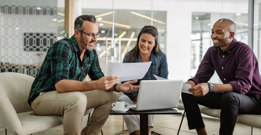 Three people smiling and reviewing documents around a table in an office.